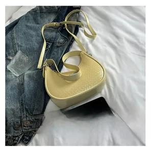 Detail of light yellow woven crescent bag with adjustable leather strap and texture
