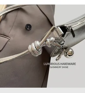Detail of silver metallic handbag with pleated texture, knot handle and ball pendant