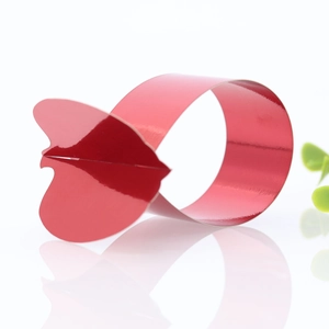 Close-up of a glossy red heart-shaped napkin ring on a reflective white surface