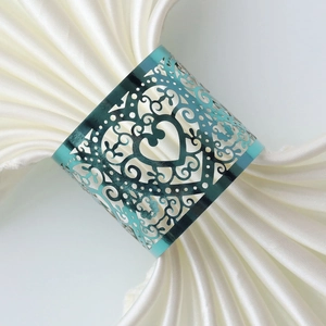 Elegant turquoise hollow heart napkin ring with floral vine patterns on white satin