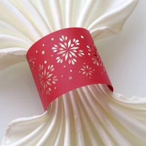 Detail of red laser-cut snowflake paper napkin ring on a white satin napkin
