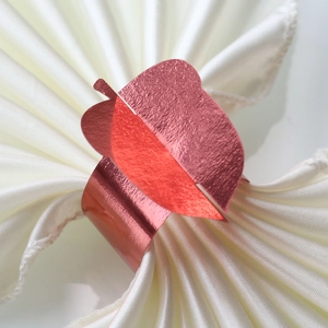 Macro detail of red metallic leaf napkin ring on elegant white silk fabric