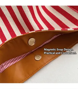 Detail of red and white striped canvas bag featuring a brown leather edge and magnetic clasp