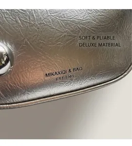 Close-up of silver crinkled leather texture and brand logo detail on the shoulder bag
