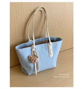 Detail of light blue faux leather tote with crocodile texture and cute bear charm