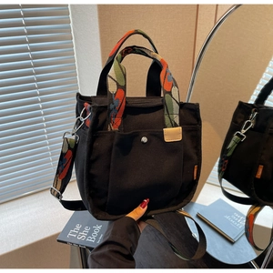 Detail of black canvas tote bag featuring colorful patterned handles and metal snap pocket
