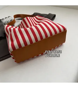 Detail view of the flat brown leather base and striped canvas of the large tote bag