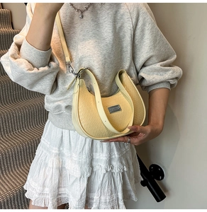 Model wearing a pale yellow woven crescent shoulder bag with smooth metal plate detail