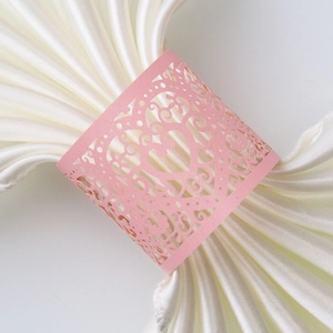 Close-up of pink laser-cut heart napkin ring with floral hollow pattern on white satin