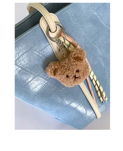 Close-up of a brown teddy bear plush charm with colorful braided rope on a blue tote bag