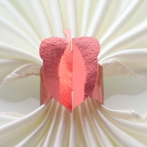 Detail of red gold napkin ring with leaf texture on folded white satin cloth