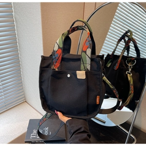 Detail of black canvas tote bag featuring colorful woven handles and a detachable strap