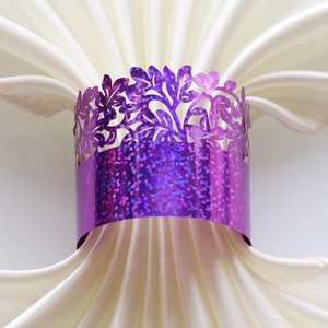 Detail of purple glitter laser-cut napkin ring with floral hollow design on white silk