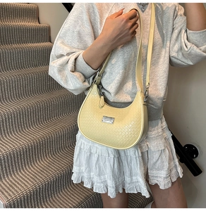Close-up of a pale yellow crescent bag with woven texture and silver metal plaque
