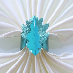 Détail du rond de serviette en forme de feuille sarcelle sur un tissu blanc