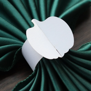 Detail of white pumpkin-shaped paper napkin ring on green satin fabric for Thanksgiving