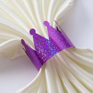 Detailed close-up of a purple glitter crown napkin ring on soft white satin fabric
