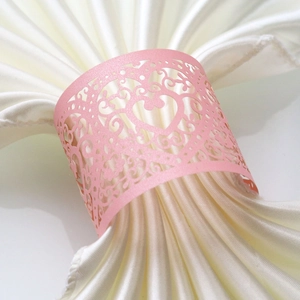 Detailed view of pink laser-cut heart napkin ring on a white silk table setting