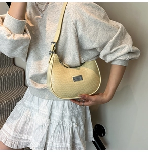 Detail of creamy yellow crescent shoulder bag with crocodile pattern on a female model