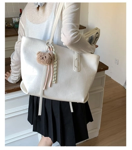 Detail of white crocodile embossed tote bag with plush bear charm on shoulder strap