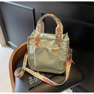 Detail of light green canvas tote bag featuring floral jacquard strap and front button pocket