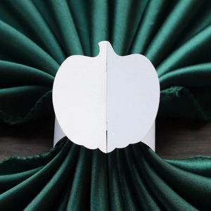 Detail of white pumpkin-shaped napkin ring on a dark green satin fabric for Thanksgiving