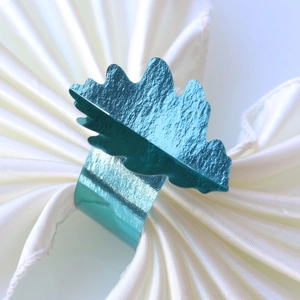 Gros plan d'un rond de serviette feuille en métal bleu sarcelle sur soie blanche