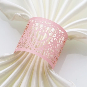 Detail of pink laser-cut heart napkin ring with floral hollow pattern on white silk