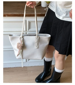 Close-up of white crocodile pattern tote bag with plush bear charm and slender straps