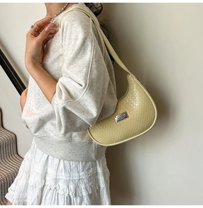 Close-up of light beige crescent shoulder bag with woven texture and silver metal logo