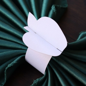 Detail of white apple-shaped paper napkin ring on dark green satin fabric background