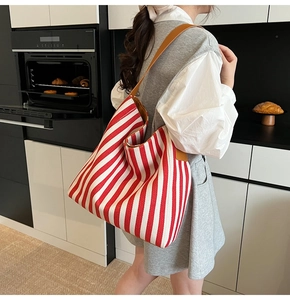 Detailed side view of a large red and white striped canvas tote with brown leather straps