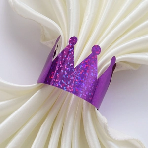 Detail view of purple glitter crown paper napkin ring on ivory satin fabric