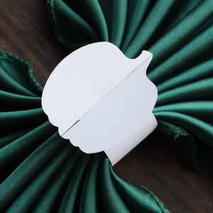 Close-up of white paper pumpkin napkin ring on elegant dark green satin backdrop
