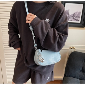 Macro detail of a light blue crescent bag with silver rabbit charm and leather texture