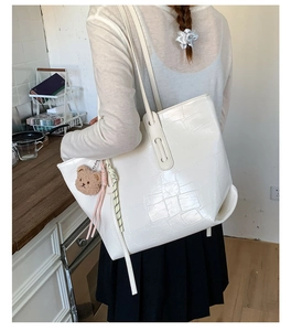 Detail of white crocodile pattern tote bag with plush bear charm and woven cord