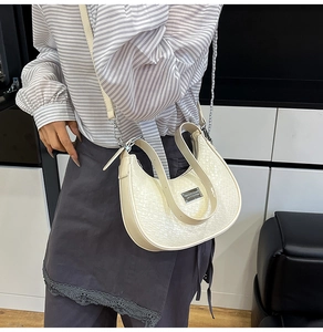 Close-up of beige woven crescent bag with adjustable shoulder strap and silver metal logo
