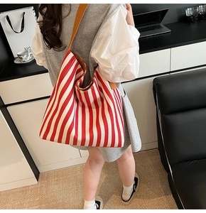 Detail of red and white striped canvas tote bag with brown leather shoulder strap on shoulder