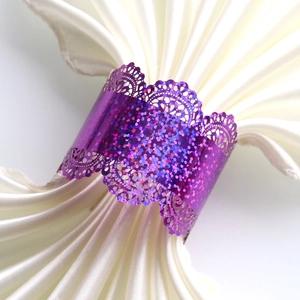 Detail of purple sequin napkin ring with laser-cut lace edges on white satin fabric