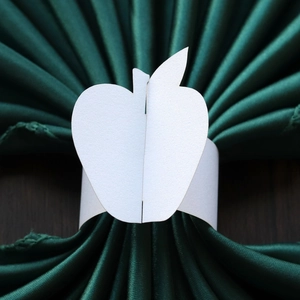 Detailed view of white apple-shaped paper napkin ring with a pearl finish on dark wood