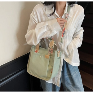 Detailed shot of green canvas tote with floral embroidered strap and front pocket