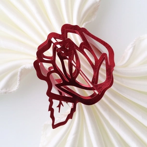 Detailed close-up of a red hollow-carved rose napkin ring on a white silk napkin