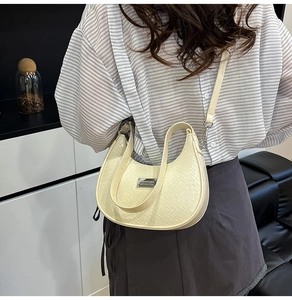 Detail of cream white half-moon bag featuring crocodile embossed texture and metal logo