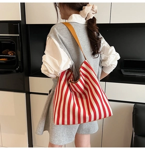 Detail of red and white striped canvas tote bag showing the leather shoulder strap on a model