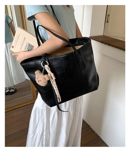 Detail of black faux crocodile leather tote bag featuring a cute bear charm and woven rope