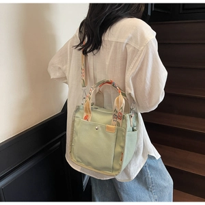 Detail of light green canvas tote with floral embroidered straps and front snap pocket