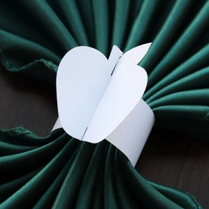 Detail of apple-shaped white cardstock napkin ring on a dark green napkin and wooden table