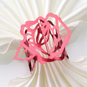 Close-up of pink metal rose napkin ring with laser-cut hollow design on white fabric