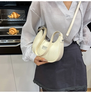 Detail of cream crescent crossbody bag with woven texture and silver metal hardware