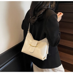 Side view of cream leather shoulder bag with gold metal buckle on a black suit model